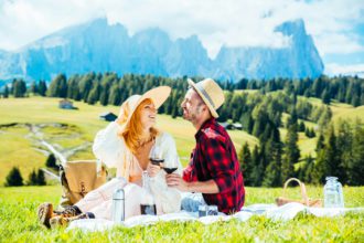 Young couple drinking red wine sitting on countryside field